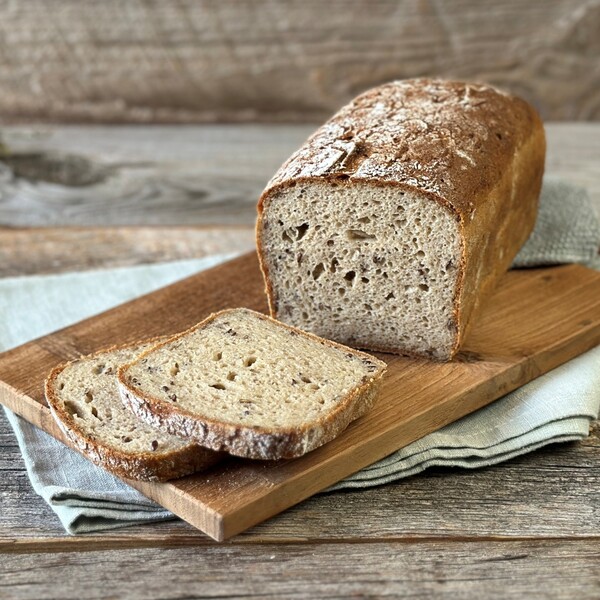 Vollwerttoastbrot mit zwei aufgeschnittenen Scheiben auf einem Holzbrett und einem grauen Tuch darunter auf einem Holztisch